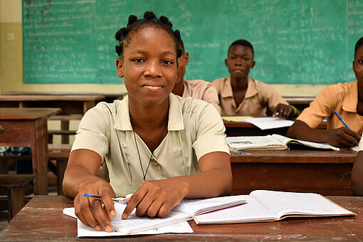 Schülerin in einer Schulklasse in Benin studiert konzentriert, mit aufgeschlagenem Notizbuch und Stift.