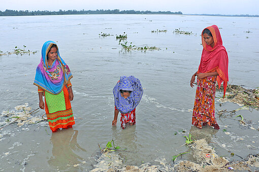Drei Frauen in bunten Kleidern stehen bis zu den Knien im Wasser