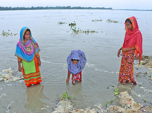 Wenn in Bangladesch die Flut kommt, werden Felder, Dörfer und auch Sportplätze überschwemmt Drei Frauen stehen bis zu den Knien im Wasser