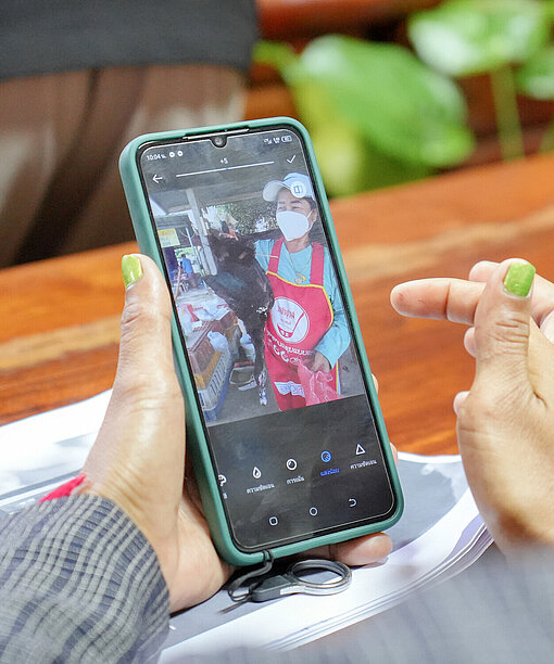 Eine Hand mit grünem Nagellack hält ein Smartphone, auf dem ein Bild von einer Frau zu sehen ist, die eine Ente hält.