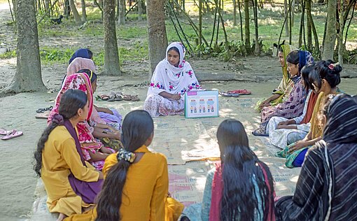 Auf Decken und Pappkartons sitzen Mädchen im Kreis unter Bäumen