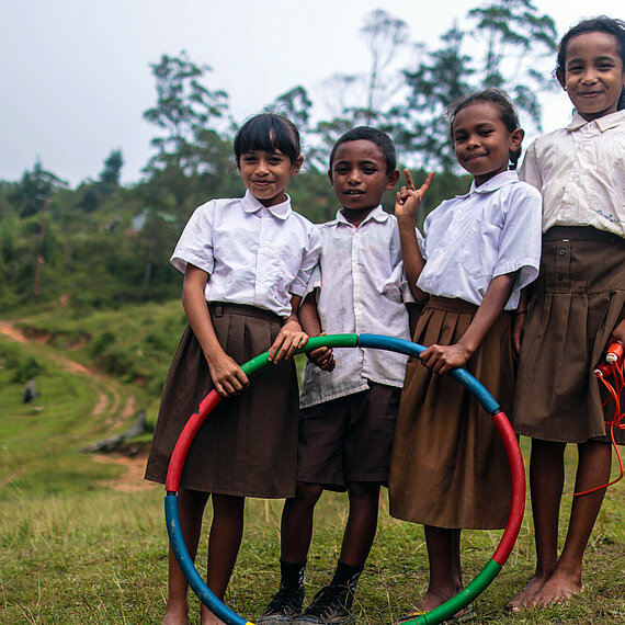 Kinder stehen mit einem Hula-Hoop-Reifen auf einer Wiese