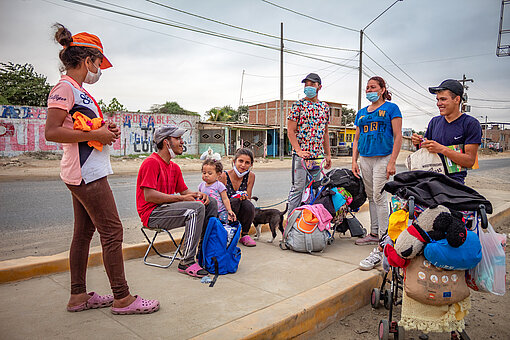 Eine sozioökonomische Krise hat Millionen Menschen aus Venezuela in die Flucht getrieben Eine Gruppe geflüchteter Menschen steht und sitzt an einer Straße und unterhält sich.