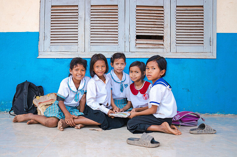 Mädchen sitzen vor einer Schule