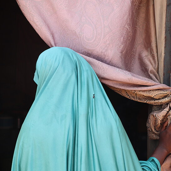 Ein Mädchen mit Kopftuch von hinten steht in einem Türrahmen
