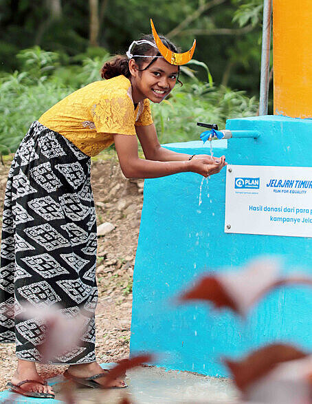 Die Menschen in ländlichen Regionen von Nagekeo warten auf eine funktionieren Wasserversorgung Ein Mädchen mit gelber Bluse und buntem Rock steht draußen an einem Wasserbrunnen