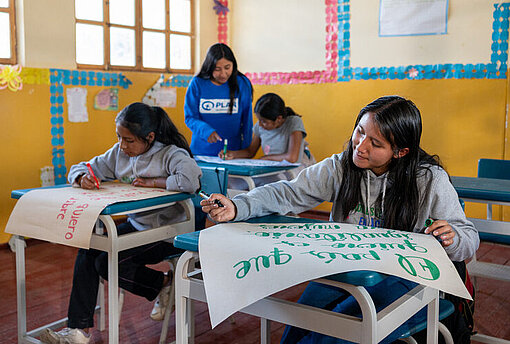 Zwei Mädchen sitzen in einem Klassenzimmer und malen Plakate