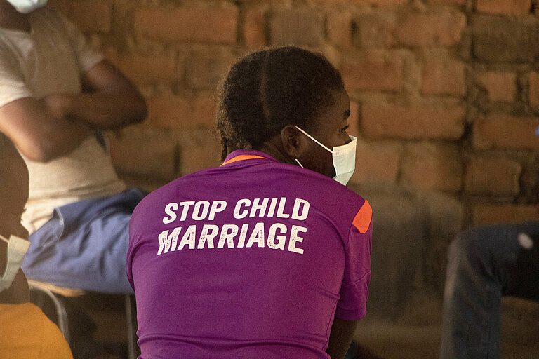 Eine junge Frau aus Sambia von hinten fotografiert, sie trägt ein T-Shirt auf dessen Rücken Stop Child Marriage (Stoppt Kinderheirat) steht