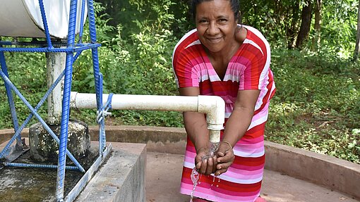 Frau wäscht sich die Hände an einem Wasserspender und lächelt in die Kamera