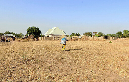 Am Rande einer sandigen Fläche stehen Häuser, vor denen eine Frau entlangläuft