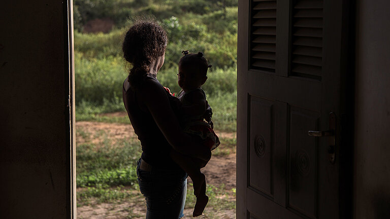 Frau mit Kind auf dem Arm steht in dunklem Türrahmen.
