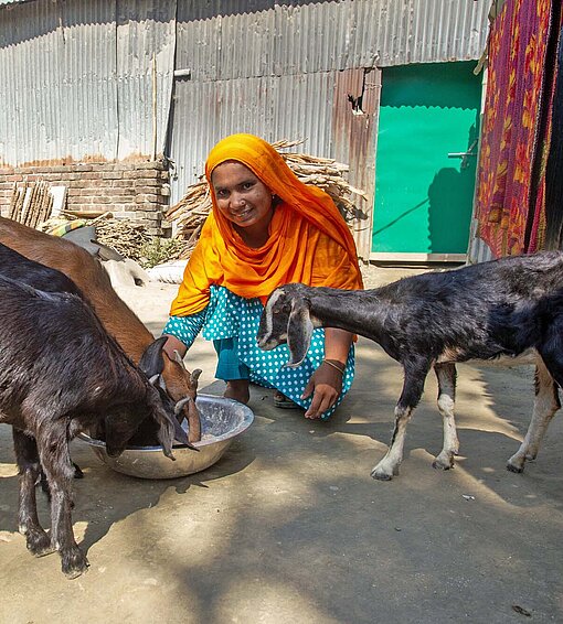 Eine Frau mit bunten Kleidern füttert Ziegen
