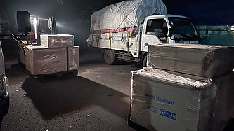 Ein Lastwagen mit Hilfsgütern, davor stehen weitere große Kartons mit Hilfsgütern