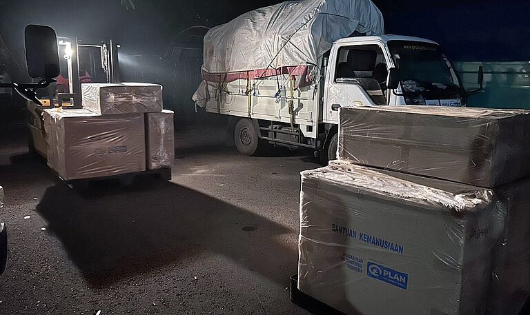 Ein Lastwagen mit Hilfsgütern, davor stehen weitere große Kartons mit Hilfsgütern