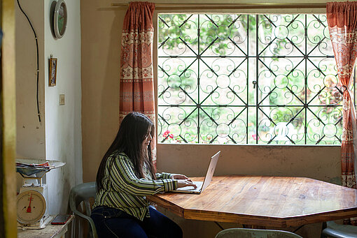 Eine junge Frau mit langen dunklen Haaren sitzt an einem runden Tisch vor einem Laptop