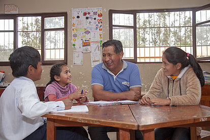 Zwei Kinder mit Schreibblöcken sitzen mit zwei Erwachsenen an einem Tisch