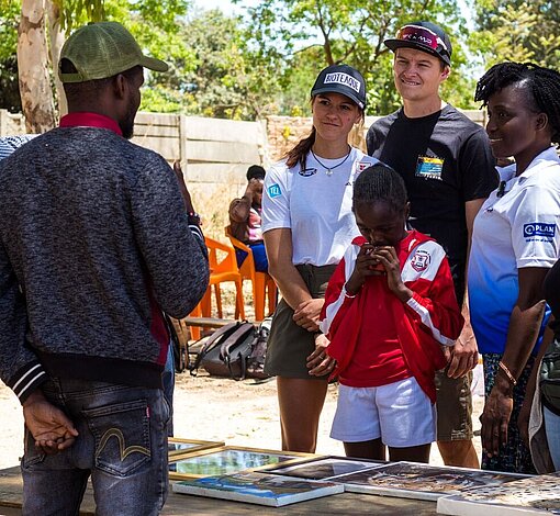 Luisa Görlich und Robin Schmid sehen sich zusammen mit Patenkind Mercy und dem Plan-Team Handwerkskunst an