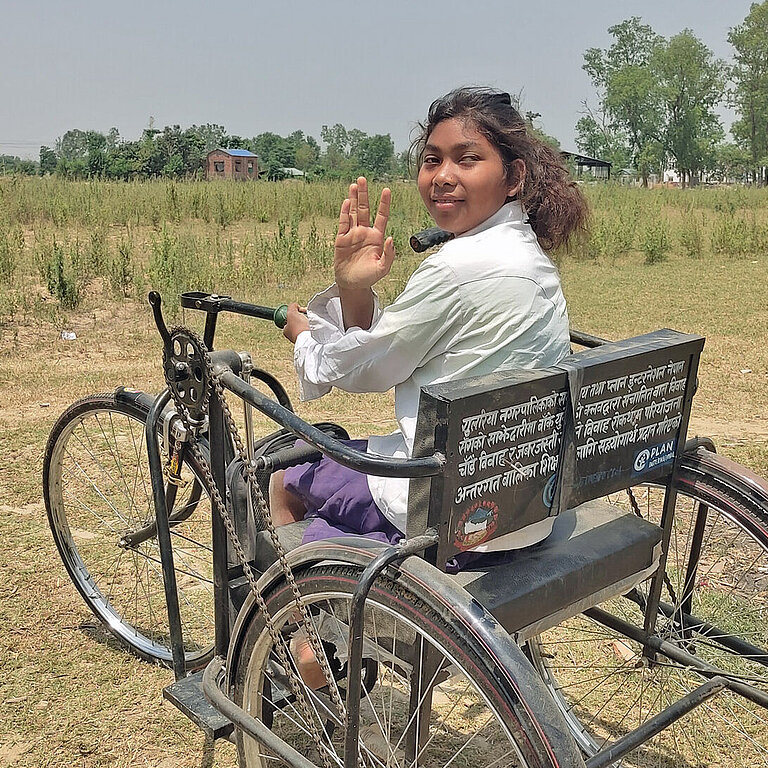 Ein Mädchen in Nepal sitzt in einem dreirädrigen Rollstuhl